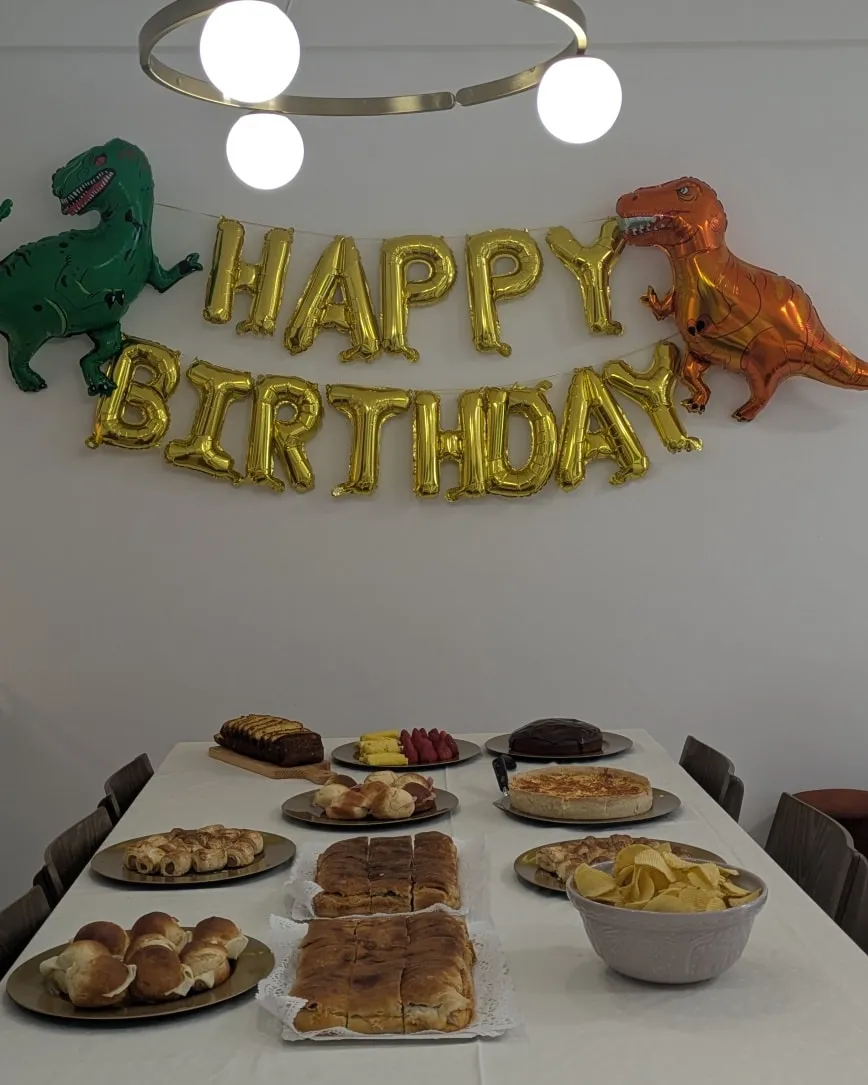 Birthday buffet table with sweets and savory food beneath balloon decorations.