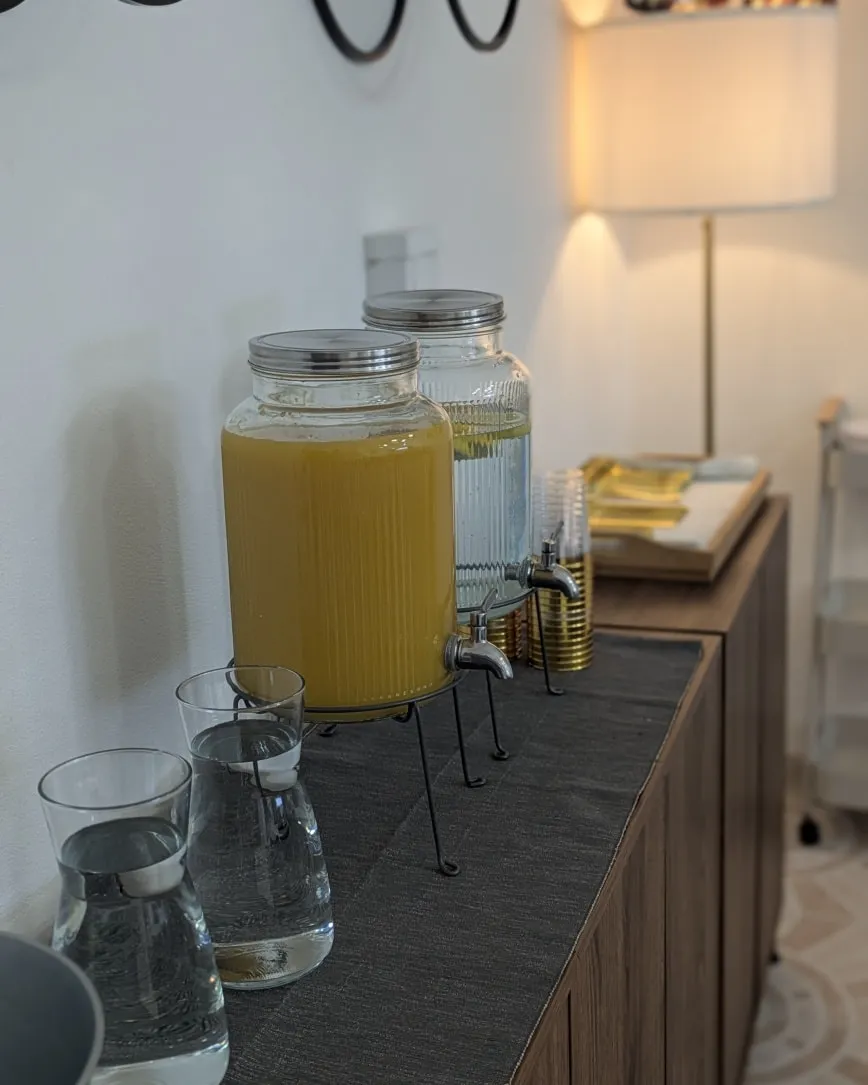 Drinks station with a dispenser, glasses, and jugs on the sideboard.